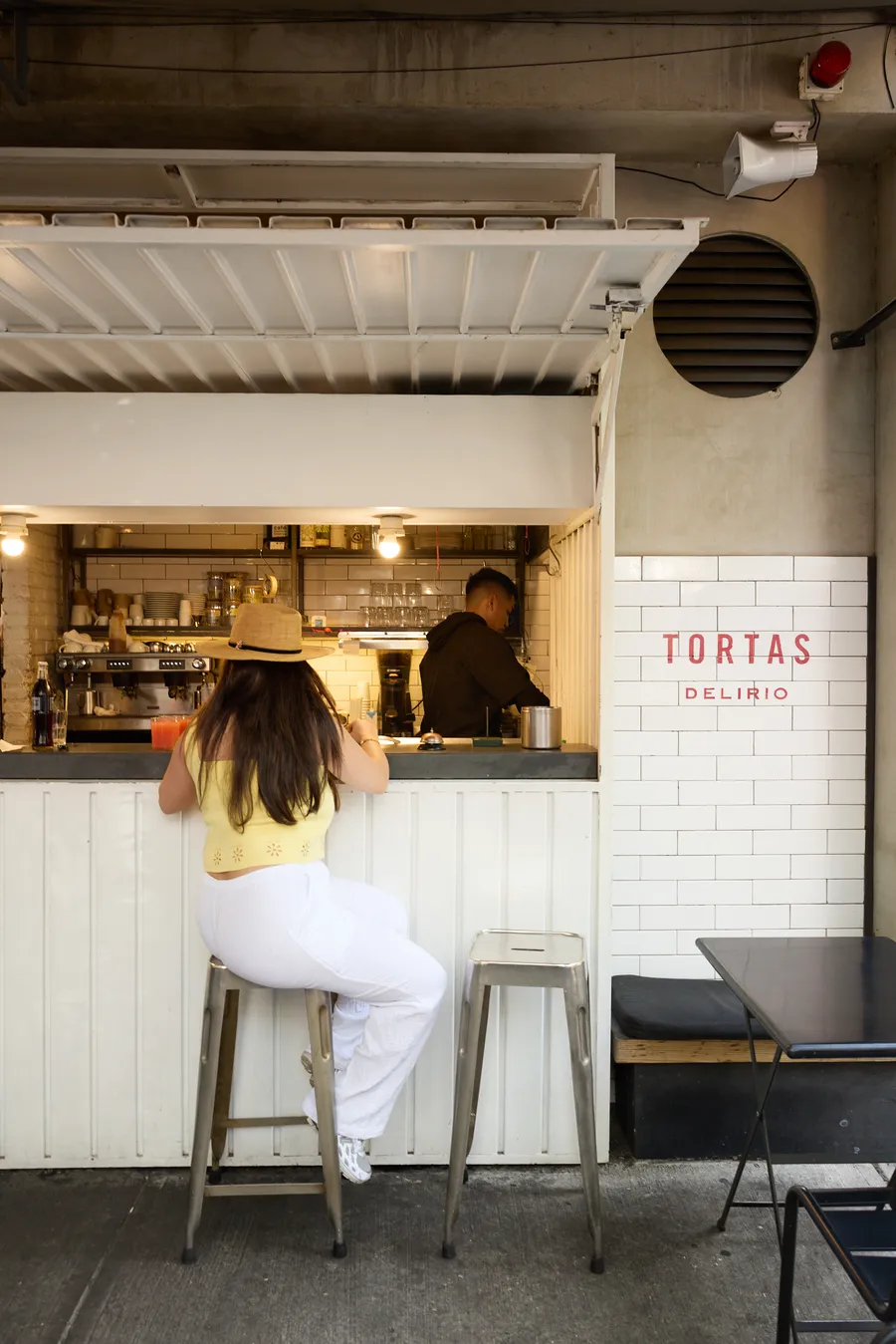 Clienta sentada en la barra de una torteria, con el letrero de la marca pintado en la pared