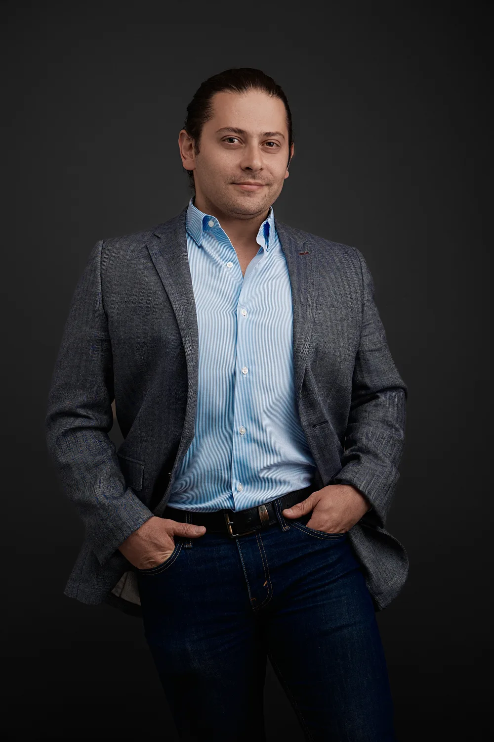 Retrato de Alfredo Ruiz, director de Pa Pronto es Tarde: saco gris, camisa azul y fondo oscuro de estudio