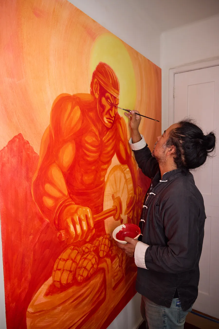 Muralista pintando con pincel la figura de un luchador en tonos naranjas sobre la pared del local