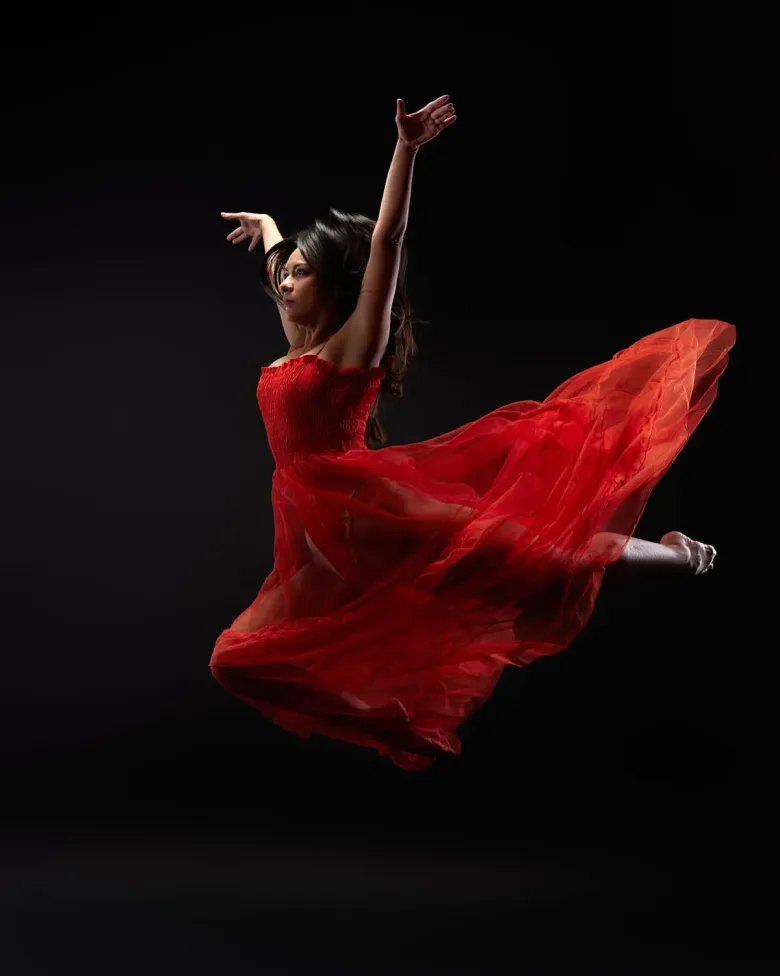 Fotografía de estudio de una bailarina con vestido rojo en pleno salto, sobre fondo negro: imagen del caso Redes Sociales